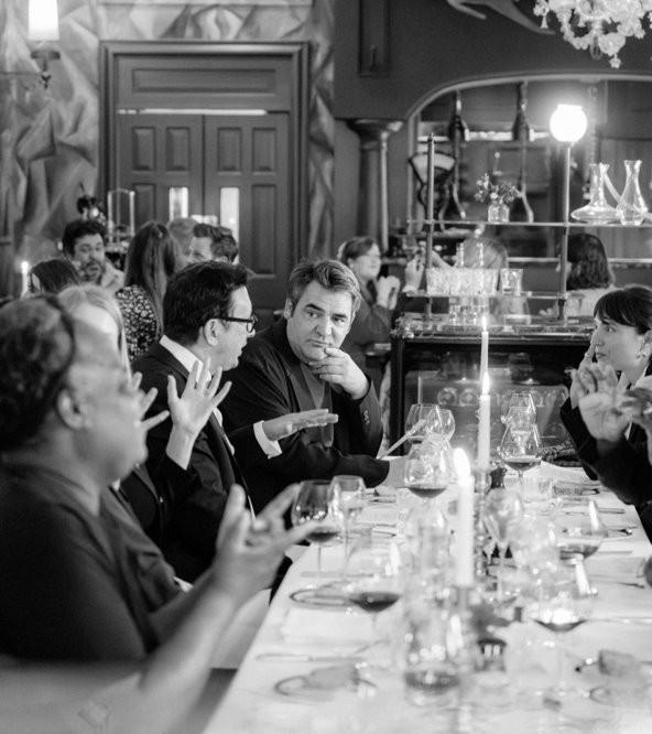 Black and white photo of guests in conversation at a dinner table.