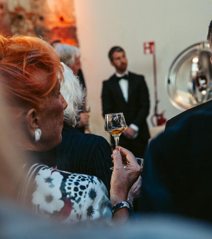Lady with dram of The Glenrothes whisky in a crowd looking at Philos